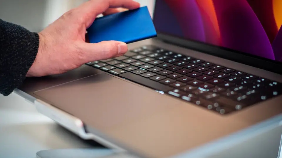 A hand holding an external drive above a laptop